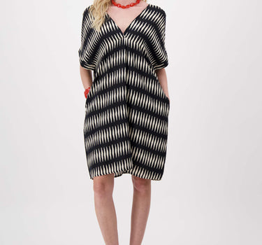 Jurk met grafische print in zwart van Zusss, model draagt een losse jurk met V-hals en rode sieraden.