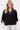 The model is wearing a black V-neck woven top with zigzag detailing by Zusss, featuring a loose fit and an elegant look.
