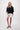 The model is wearing a black V-neck woven top with zigzag detailing by Zusss, a loose-fitting V-neck top.