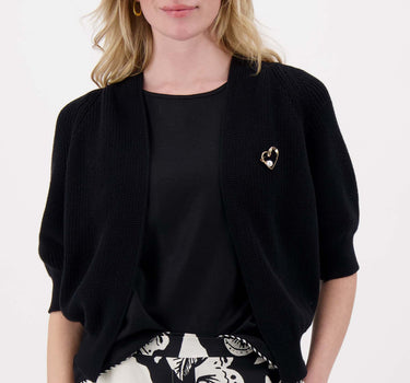 Model draagt zwart vest met vleermuis mouwen met broche van Zusss, casual en chic met gouden broche.