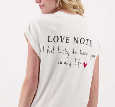 Off-white T-shirt with rolled-up sleeves and "love note" print by Zusss; the model is showing the text on the back and wearing red pants.