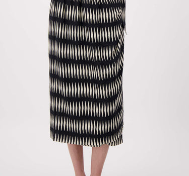 The model is wearing a black wrap skirt with a graphic print by Zusss, featuring a bow detail on the side.