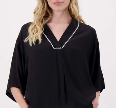 The model is wearing a black V-neck woven top with zigzag detailing by Zusss, featuring a loose fit and an elegant look.